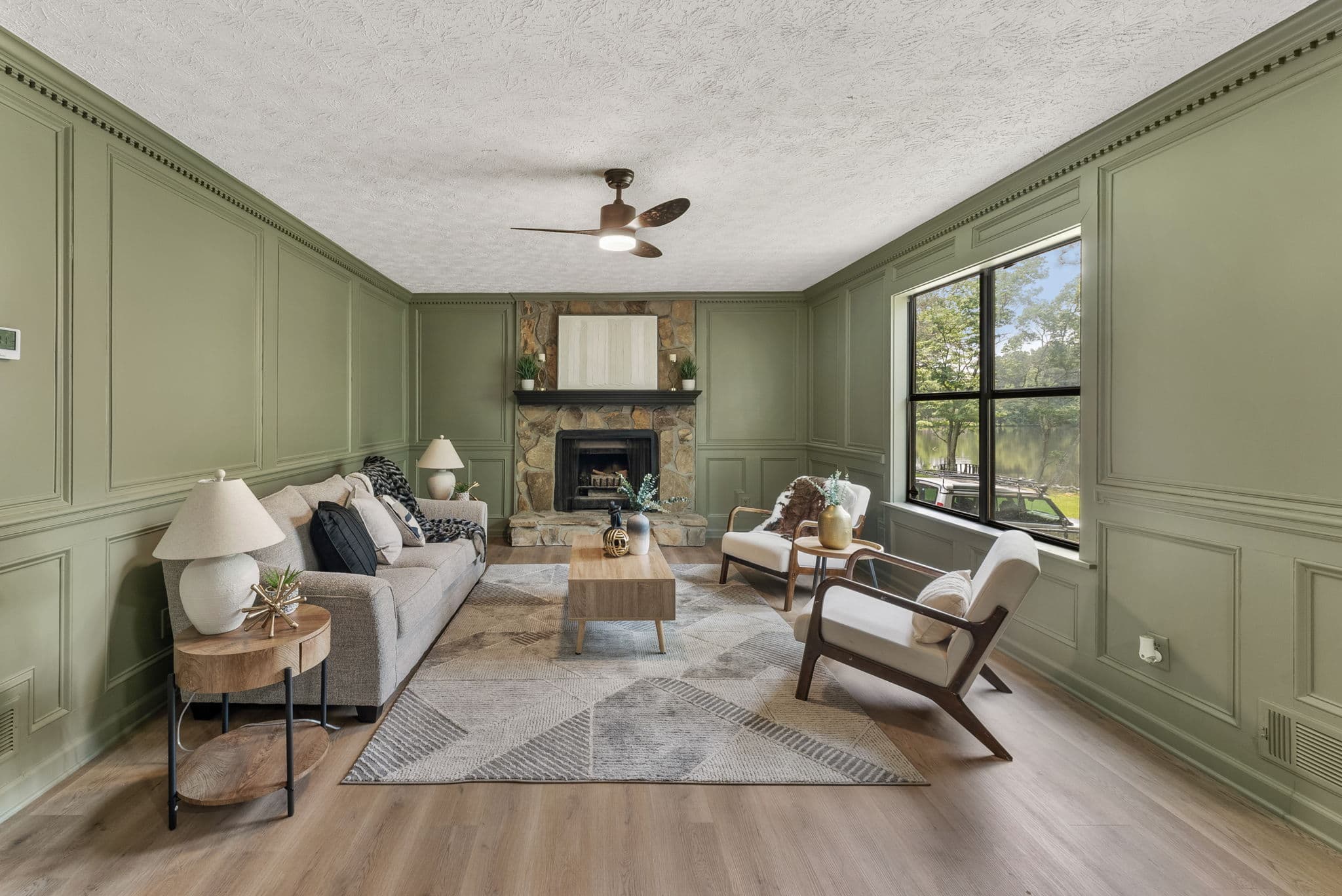After: living room with sage green paneling, stone fireplace and new flooring
