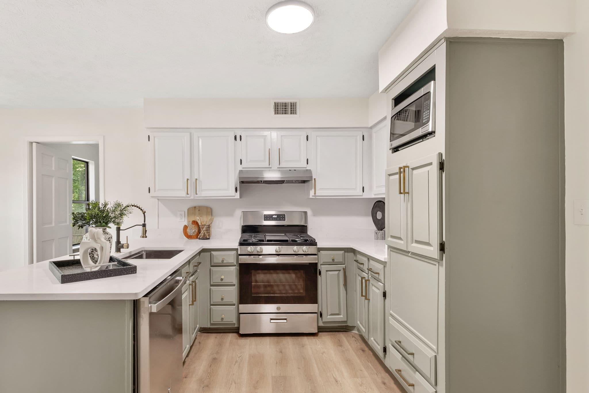 After: renovated kitchen with white and sage cabinets, quartz counters and new appliances