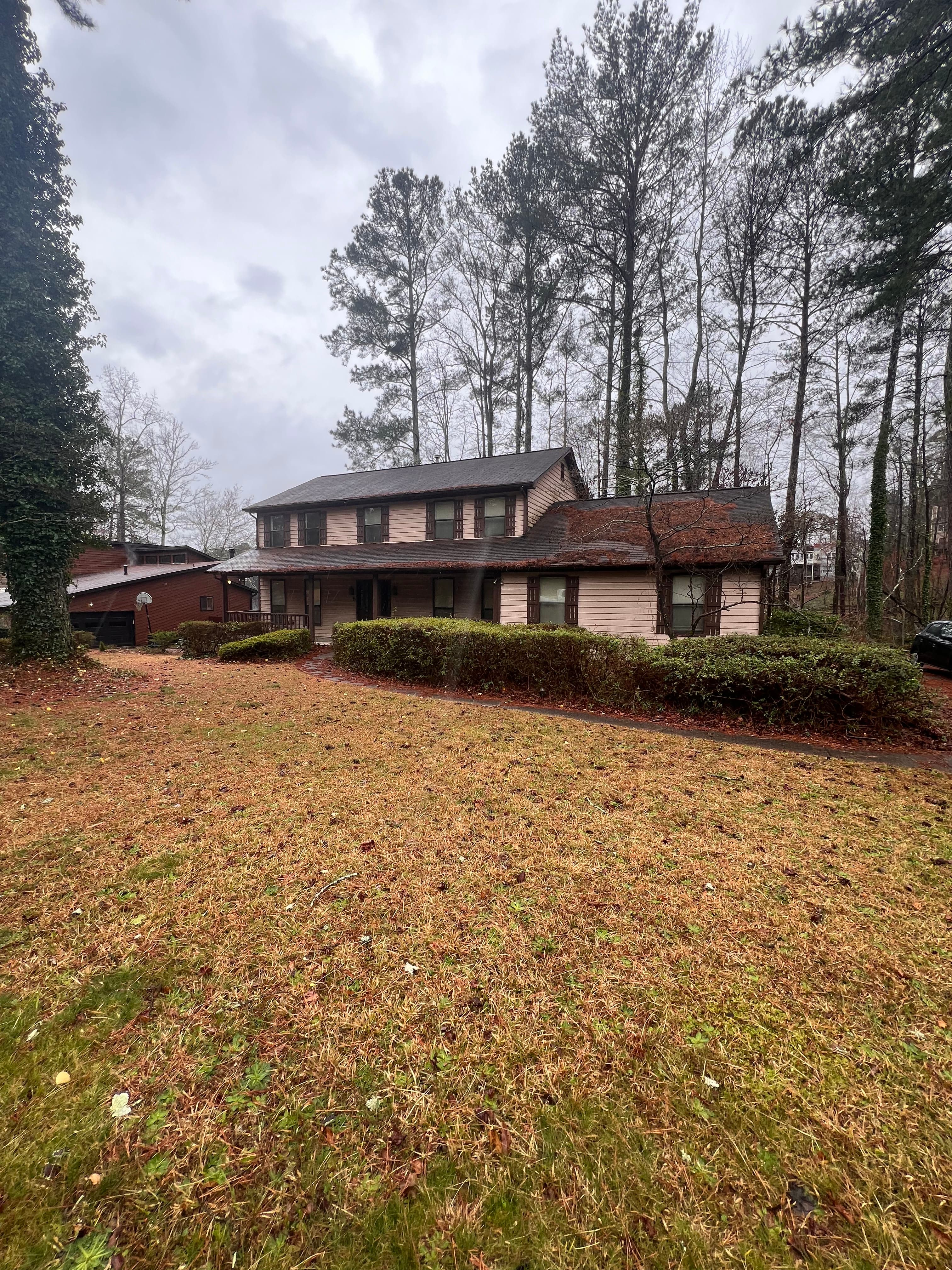 Before: original front exterior with faded siding and overgrown hedges